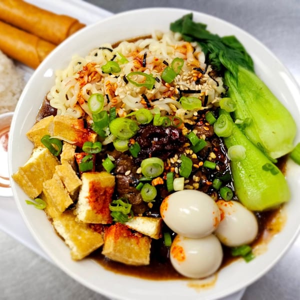 A Filipino noodle dish with bok choy, tofu, quail eggs, and green onions, served with lumpia.
