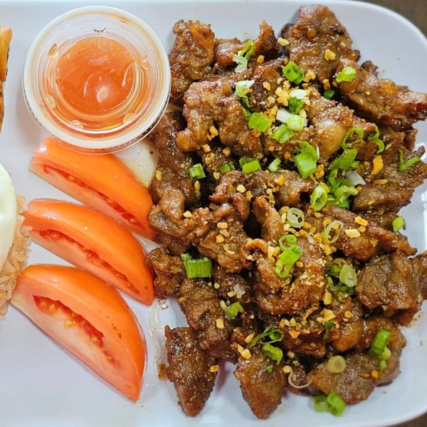 Filipino beef tapa with chopped green onions, garlic bits, tomato slices, and a side of sauce.