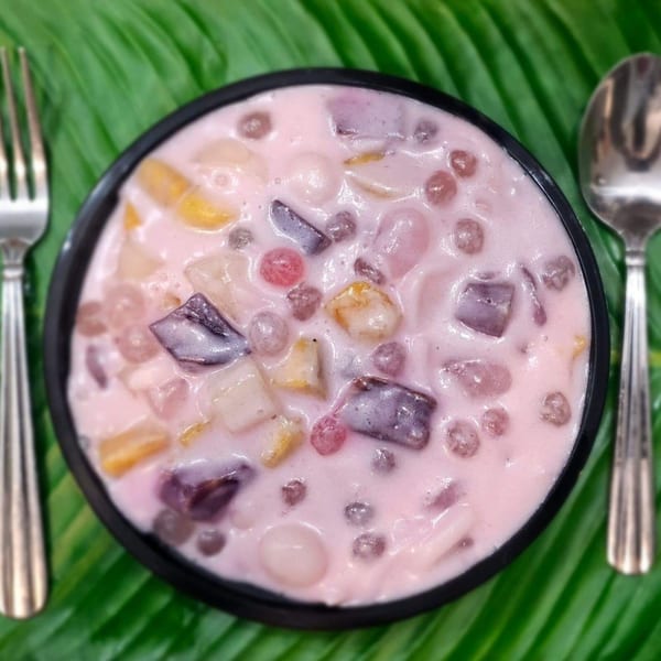 A black bowl of Kusinera Filipino Cuisine's pink Buko Salad with fruit and tapioca, on a banana leaf.