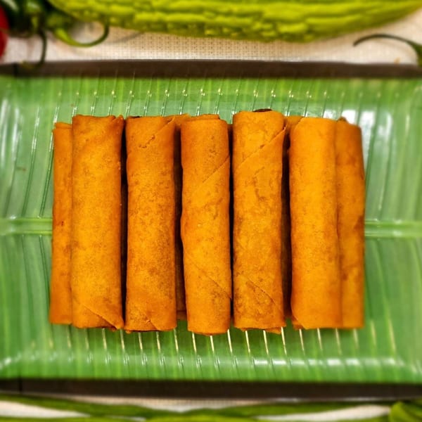Golden-brown Filipino lumpia rolls arranged neatly on a vibrant green banana leaf.