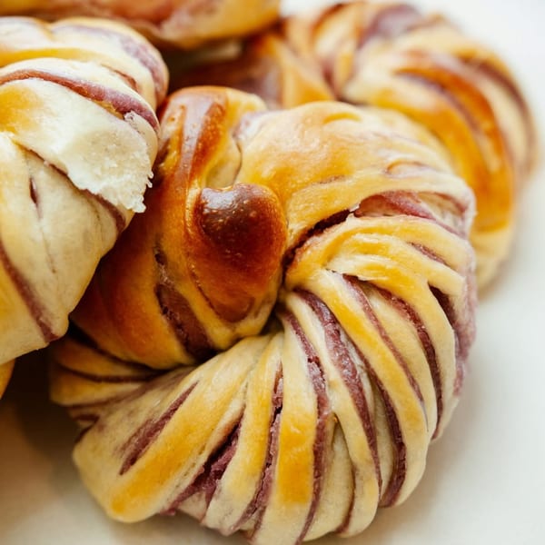 Close-up of golden-brown Filipino ube cheese pandesal, twisted with purple ube filling visible.