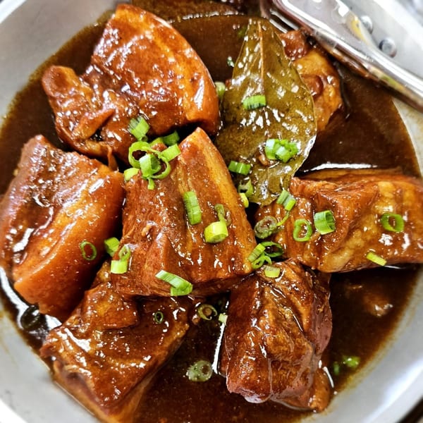 Filipino pork adobo with bay leaves and green onions in a rich, dark sauce.